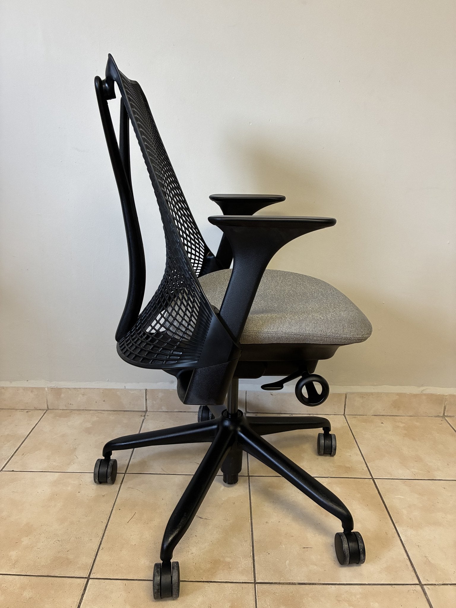 Silla de oficina Herman Miller Sayl pre-owned, respaldo negro y asiento gris, vista lateral sobre piso de azulejo.