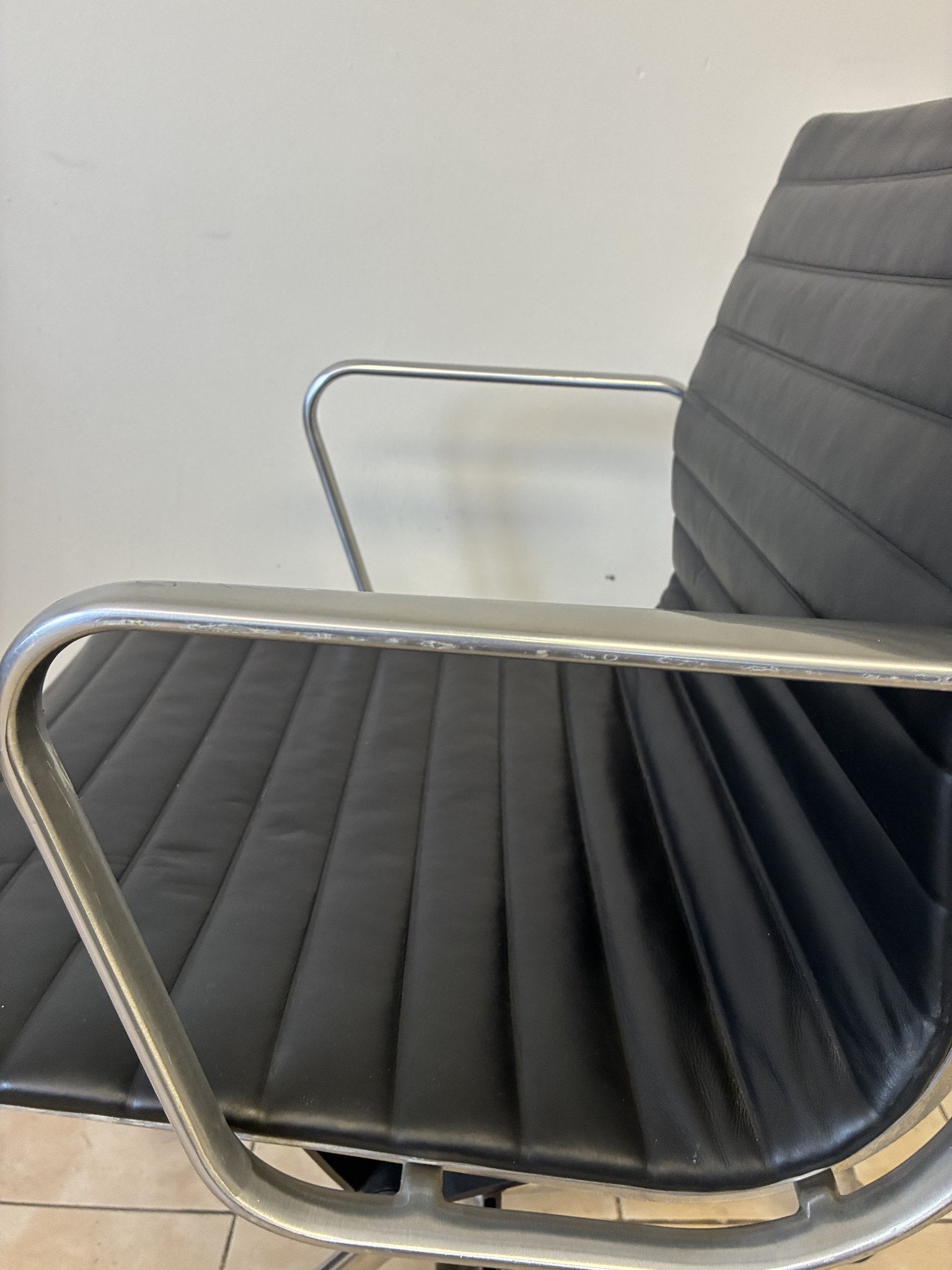 Silla Eames Herman Miller preowned de piel negra, vista lateral del asiento y respaldo con brazos metálicos.