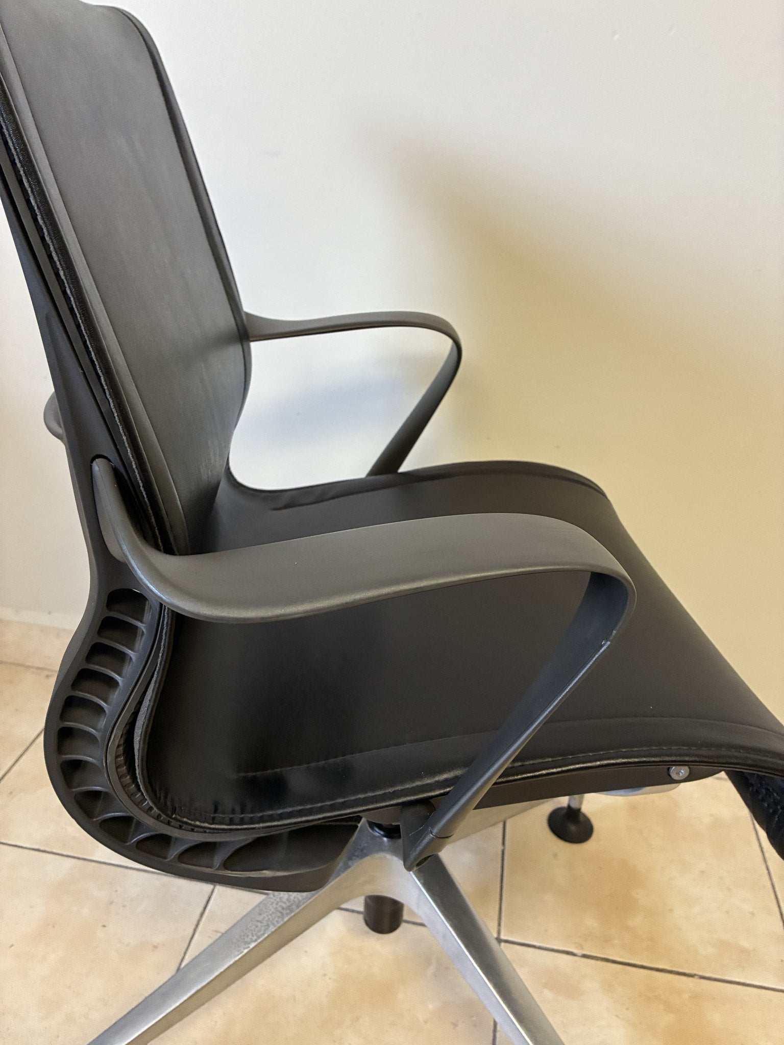 Silla de oficina Herman Miller Setu fija preowned, piel negra, vista lateral que muestra los brazos y la base.