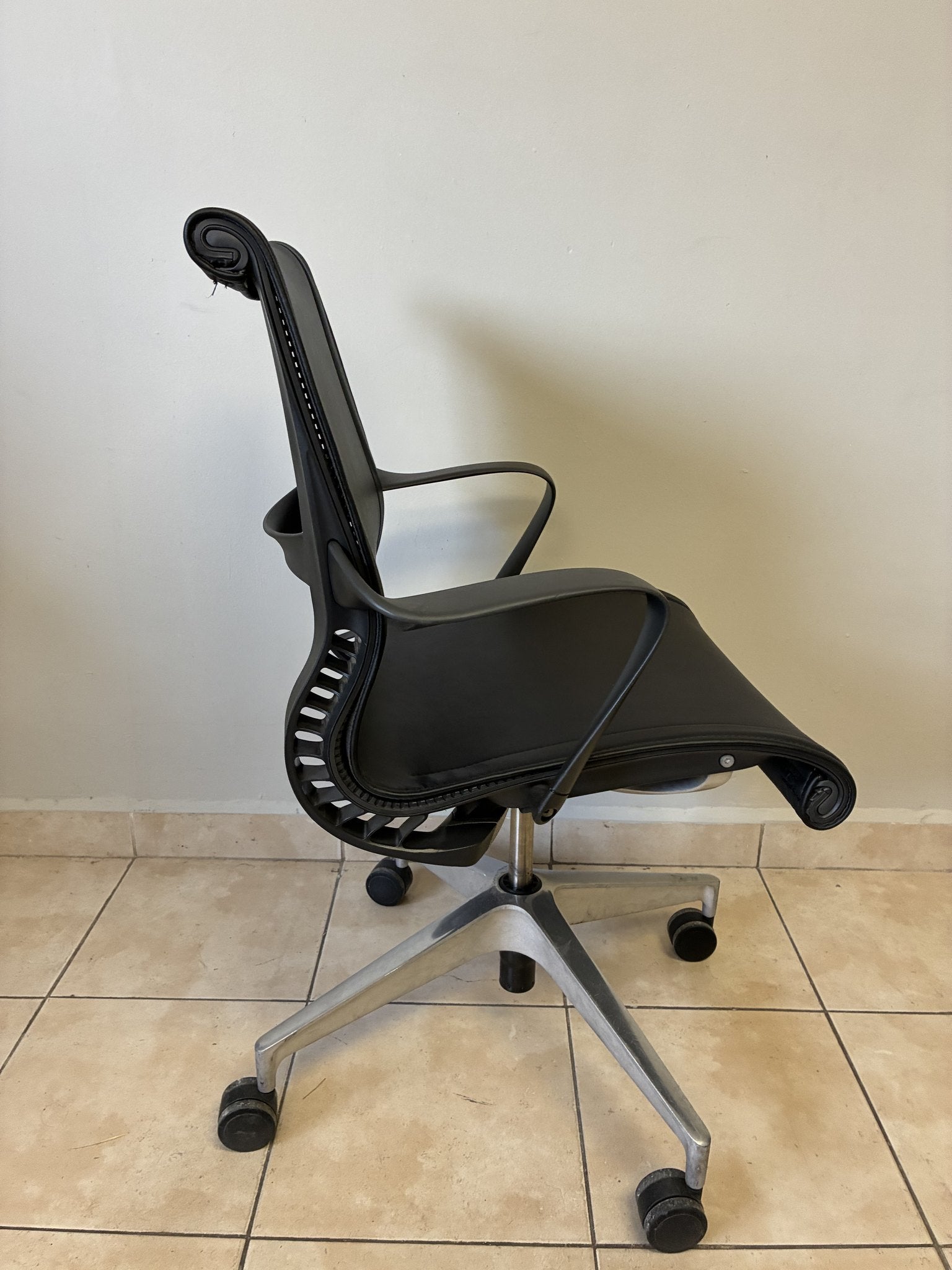 Silla de oficina Herman Miller Setu de piel negra, vista lateral. Base de aluminio con ruedas.
