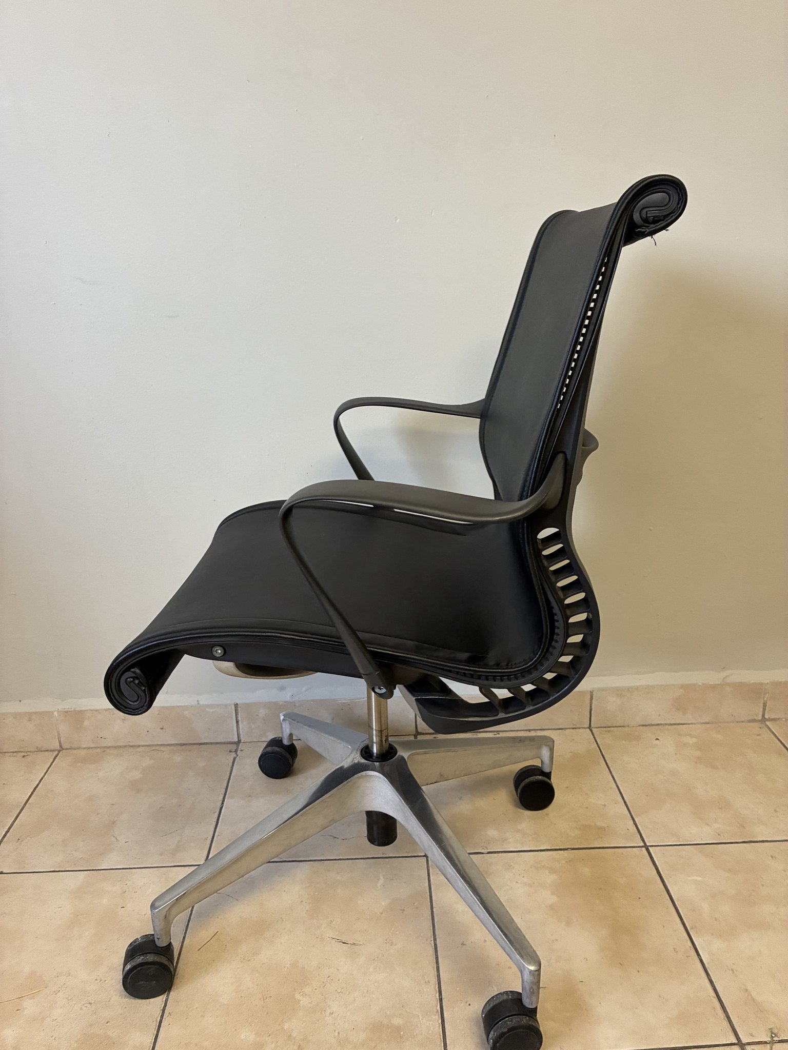 Silla de oficina Herman Miller Setu de piel negra, vista lateral con base de cinco ruedas y respaldo curvo.