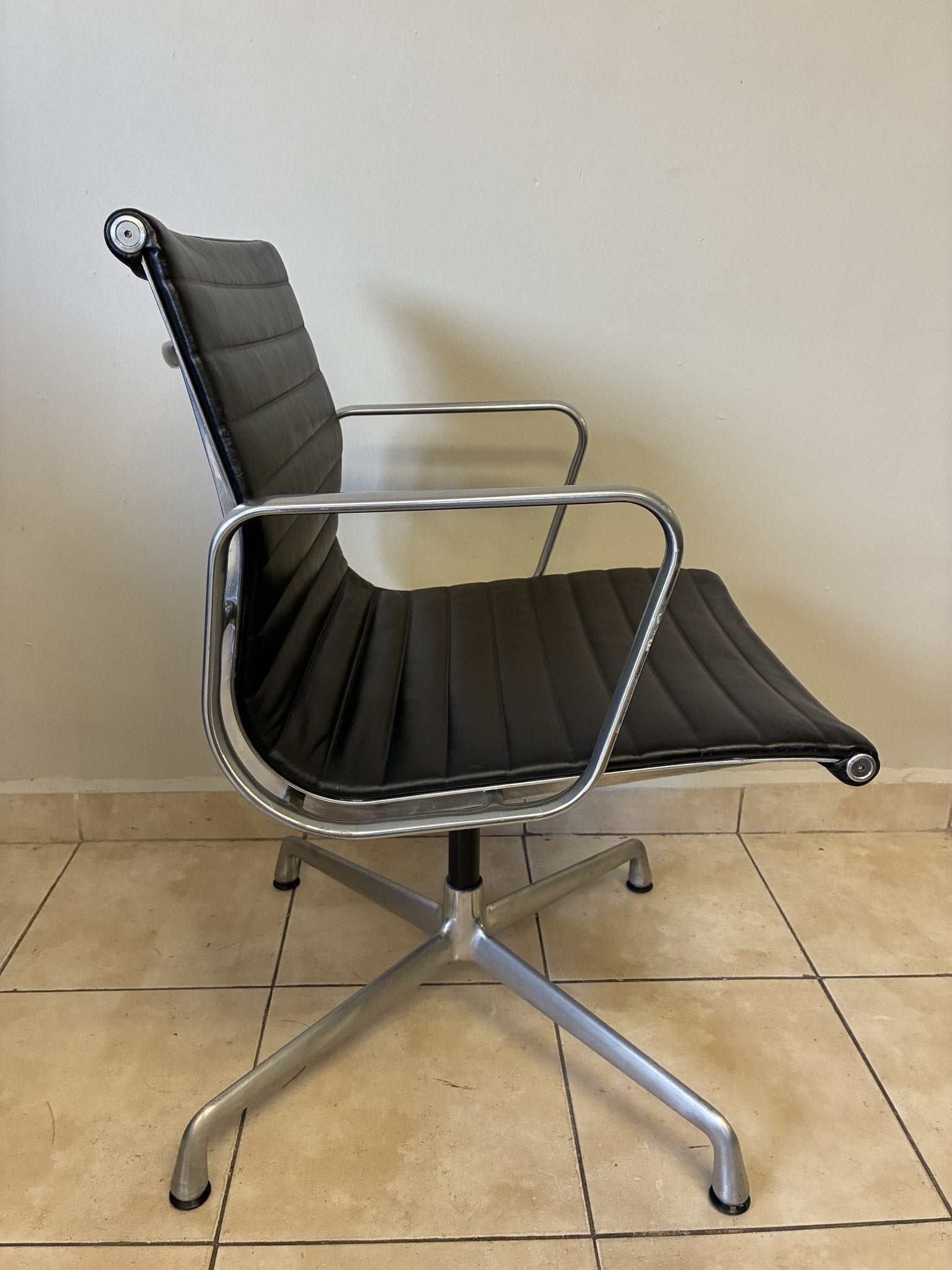 Silla Eames Herman Miller preowned de piel negra, con base fija de aluminio pulido, vista lateral en un interior.