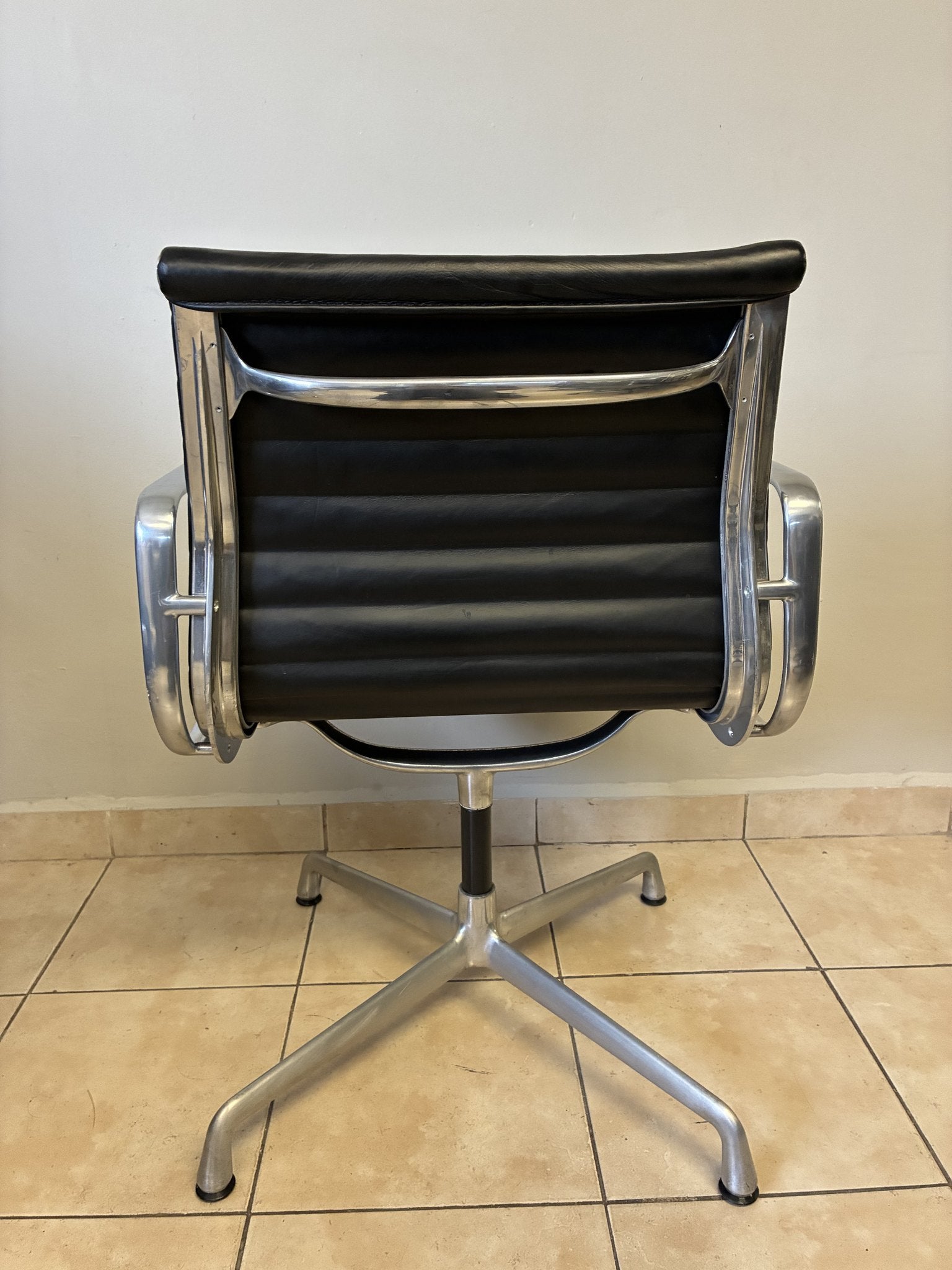 Silla ergonómica Eames Herman Miller de piel negra, vista trasera. Base de aluminio y diseño fijo.