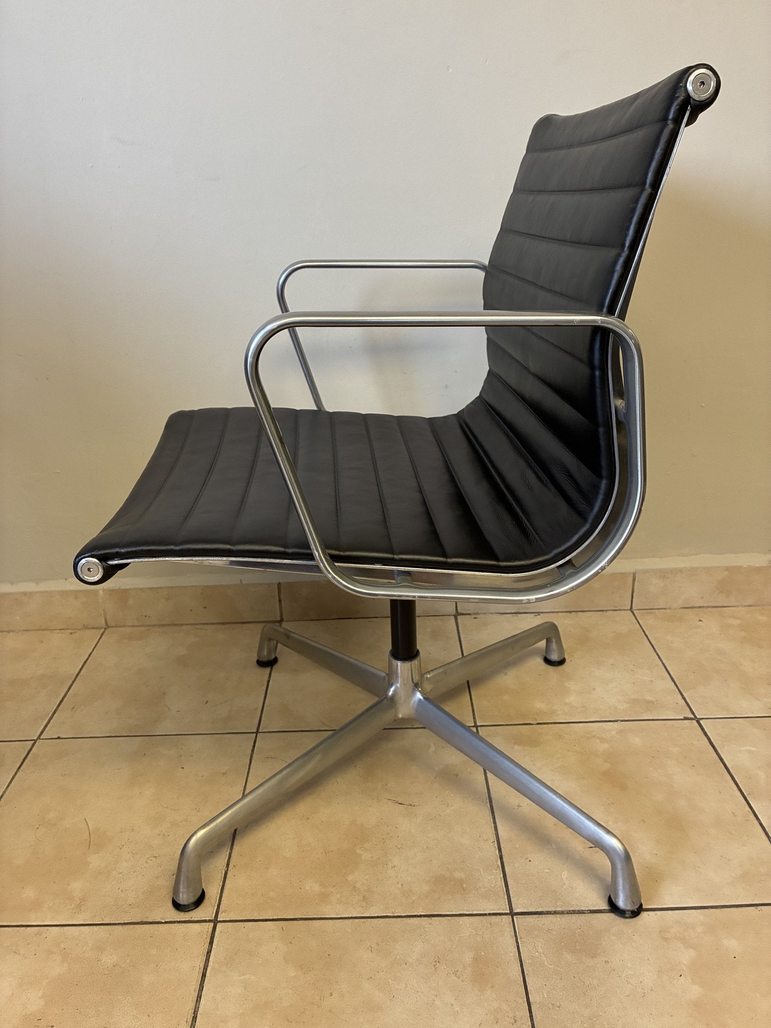 Silla ergonómica Eames Herman Miller preowned, de piel negra con base fija de aluminio, vista lateral.