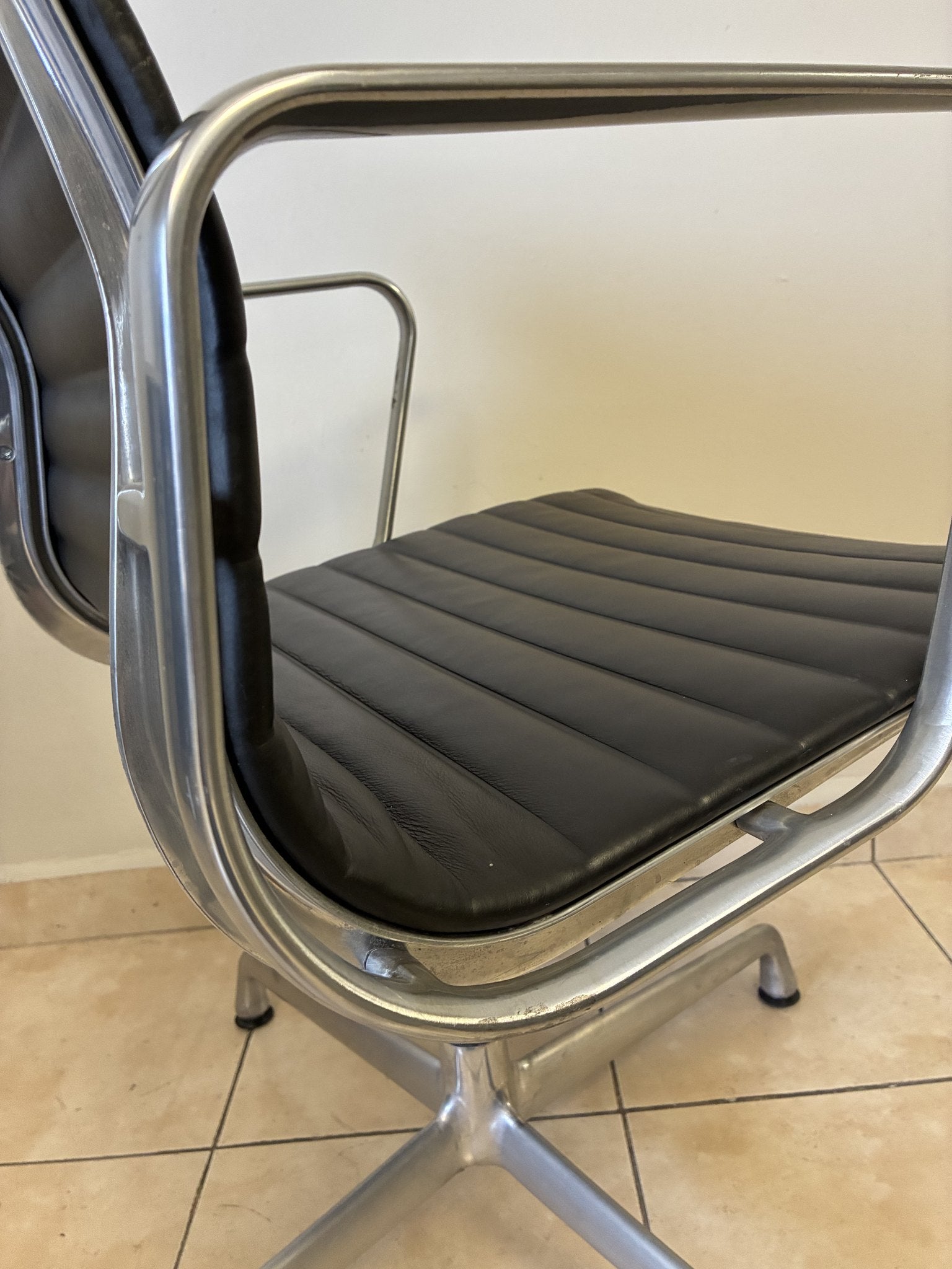 Silla Eames Herman Miller fija preowned de piel negra, vista lateral que muestra el asiento y estructura de aluminio.