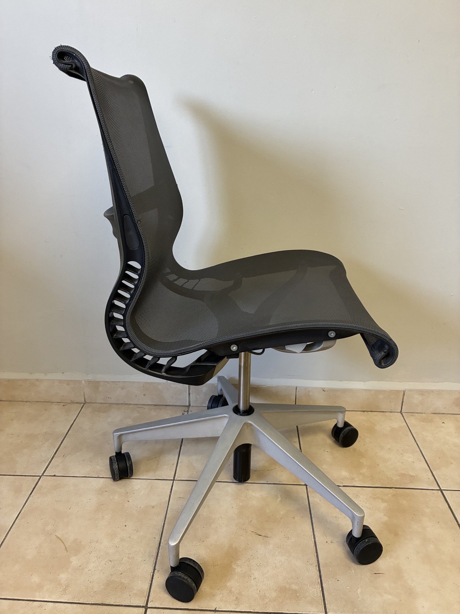 Silla de oficina Herman Miller Setu preowned, color gris oscuro, sin brazos, vista lateral sobre piso de azulejo.