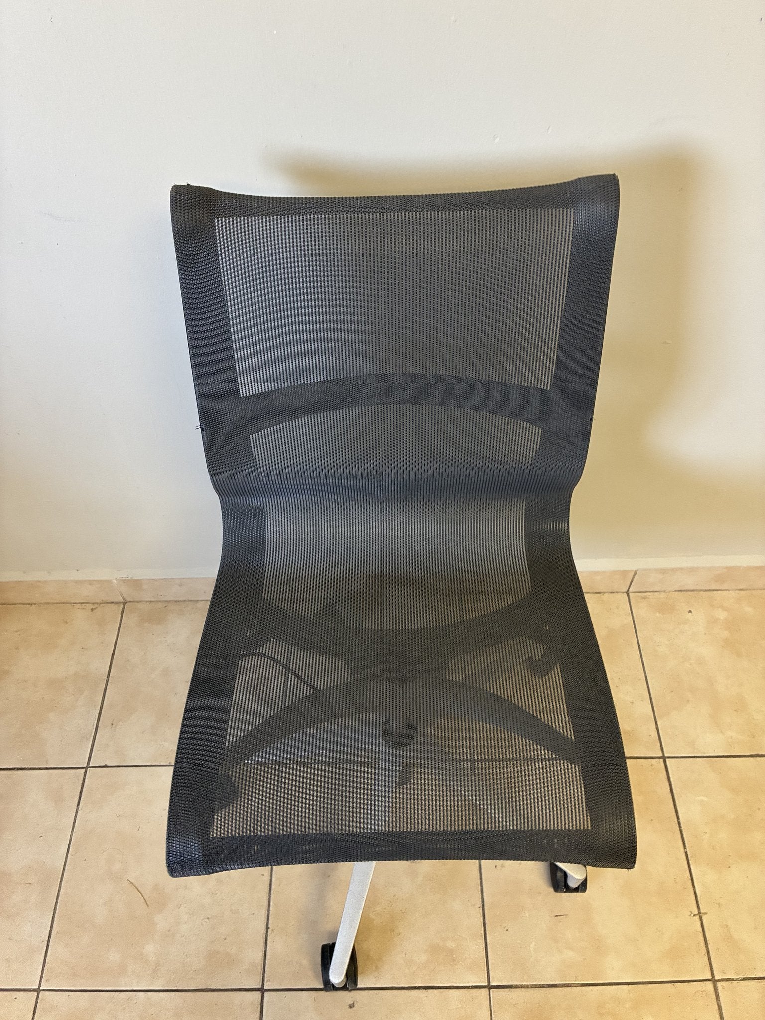 Silla de oficina Herman Miller Setu sin brazos, color gris oscuro, vista frontal completa sobre piso de azulejos.
