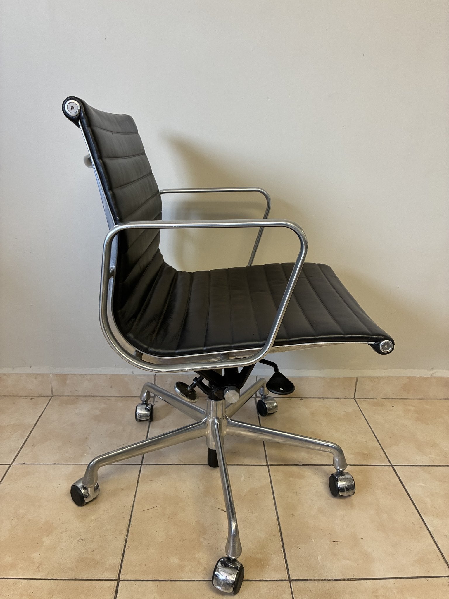 Silla ergonómica Herman Miller Eames de piel negra, vista lateral. Base de aluminio con ruedas.