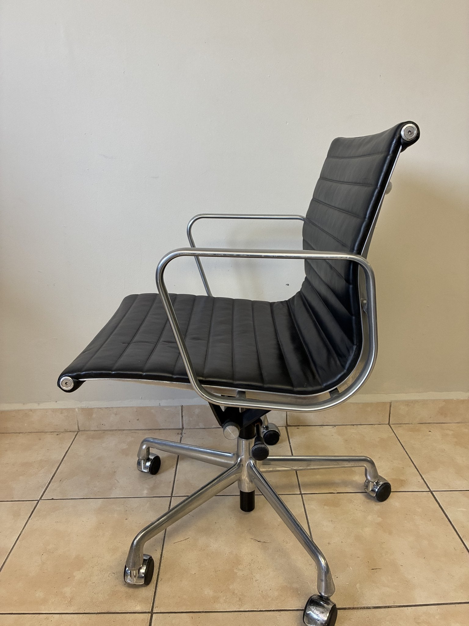 Silla ergonómica Herman Miller Eames de piel negra, vista lateral, con estructura de aluminio pulido y ruedas.