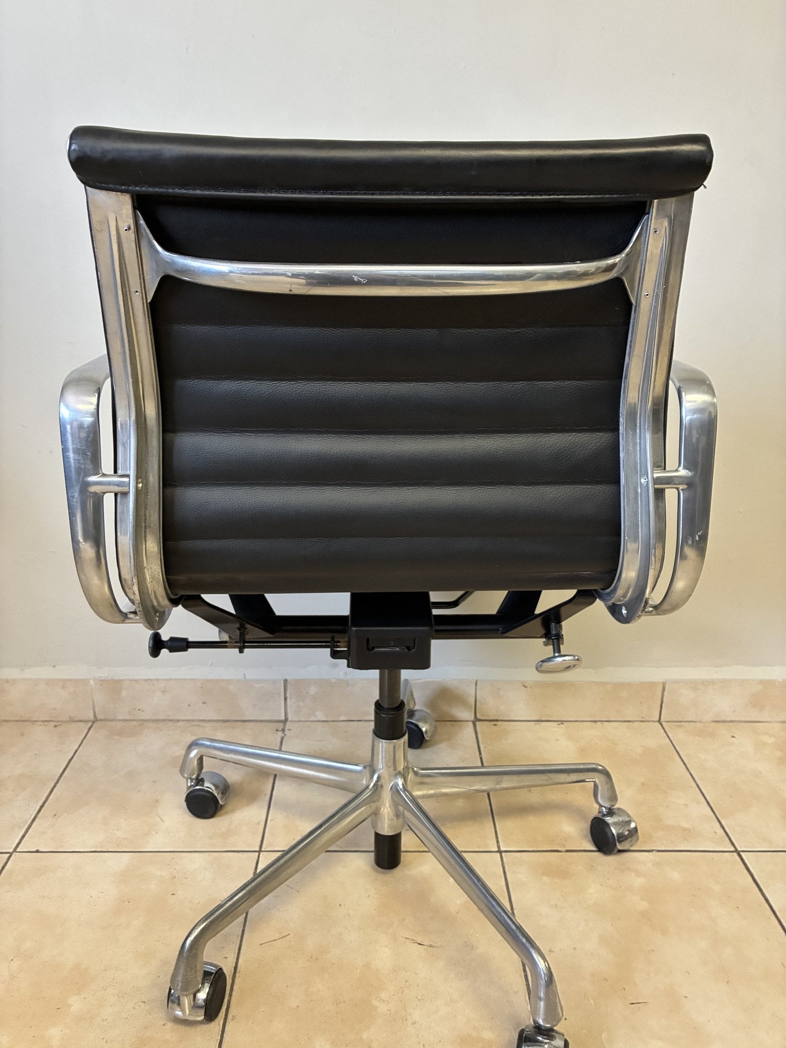 Silla ergonómica Herman Miller Eames de piel negra, vista trasera completa, con base de metal y ruedas.