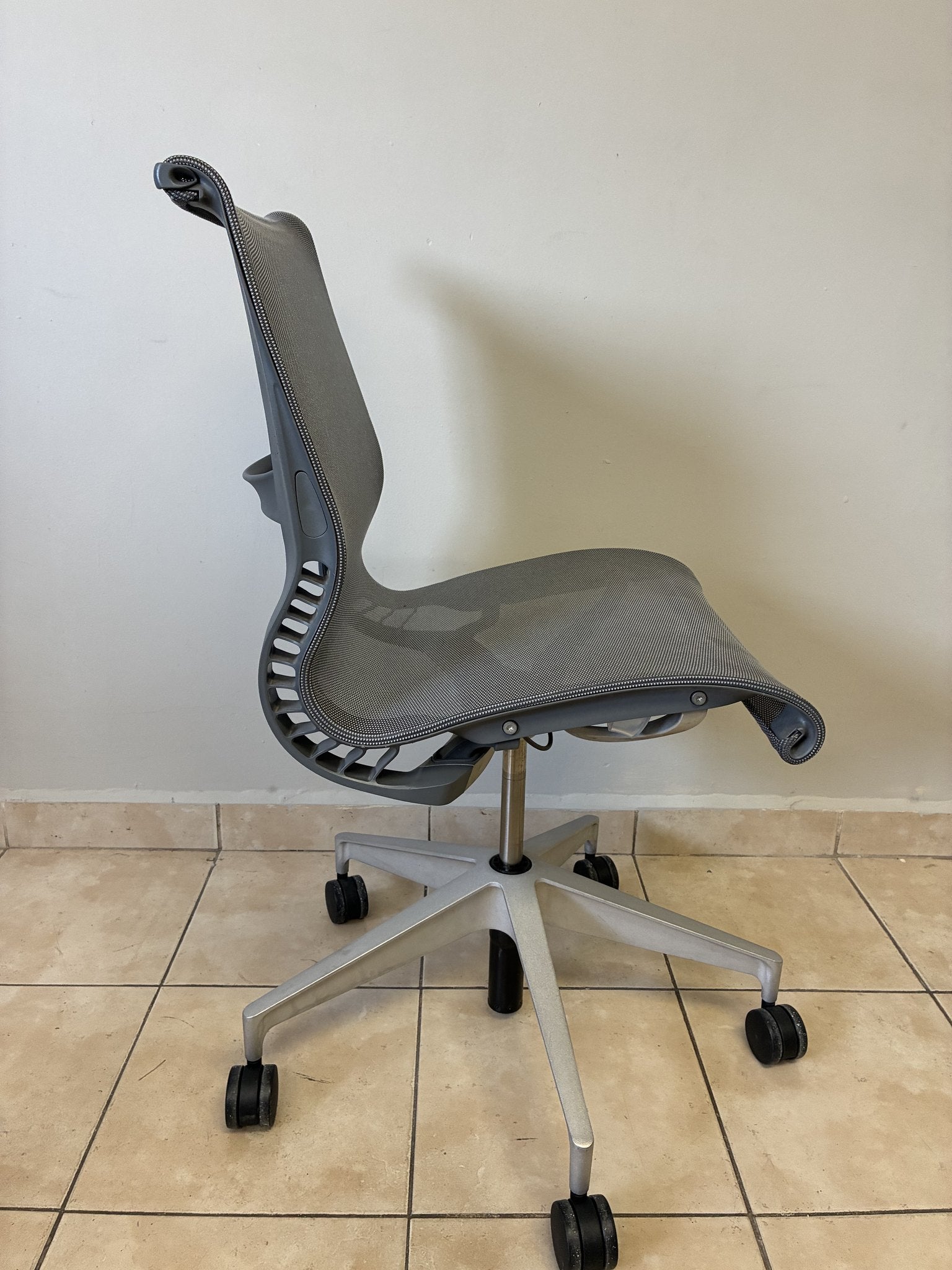 Silla de oficina Herman Miller Setu pre-owned, sin brazos, en color gris claro, vista lateral sobre piso de azulejos.