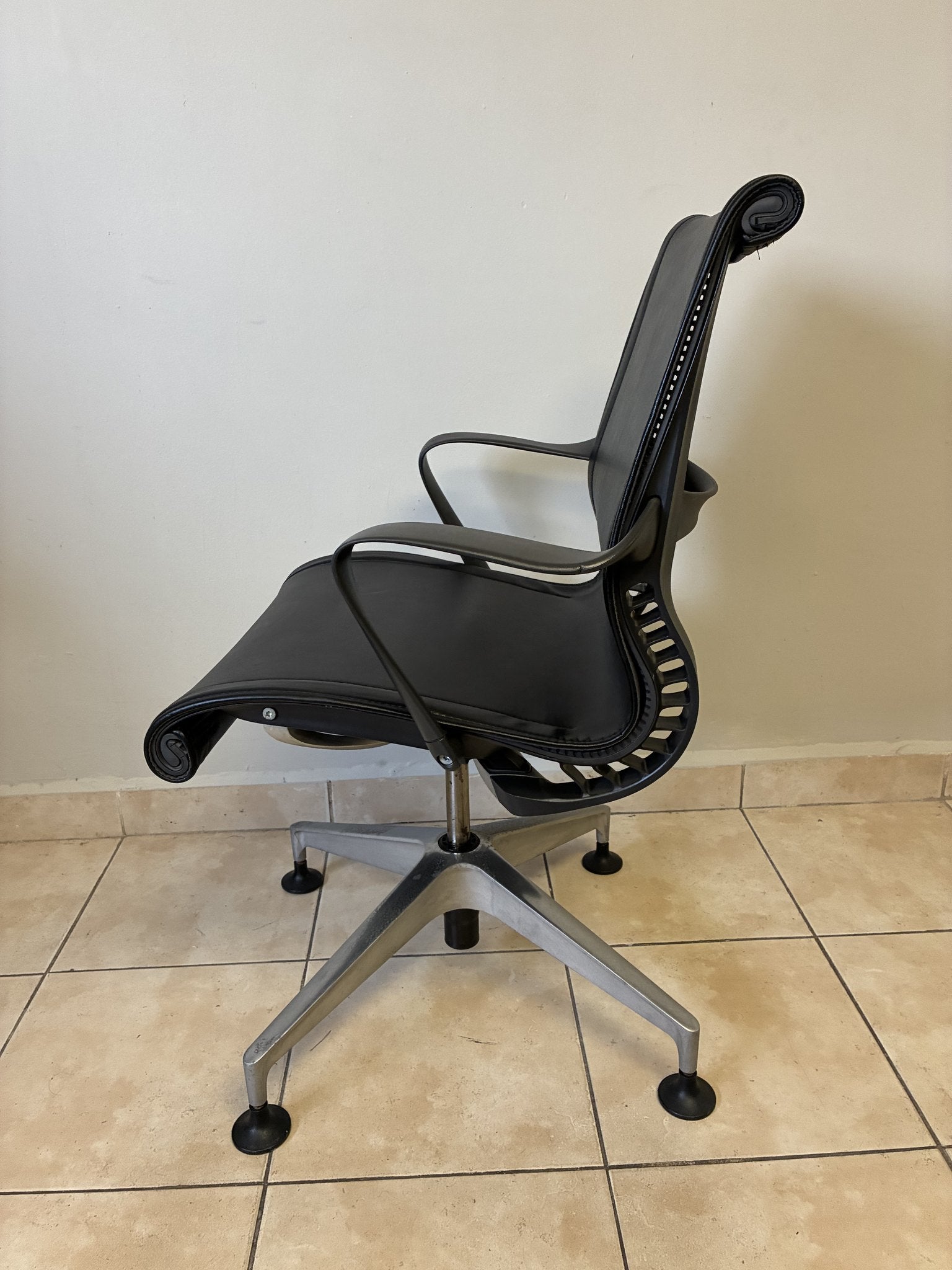 Silla de oficina Herman Miller Setu fija pre-owned, de piel negra, vista lateral sobre piso de azulejo.