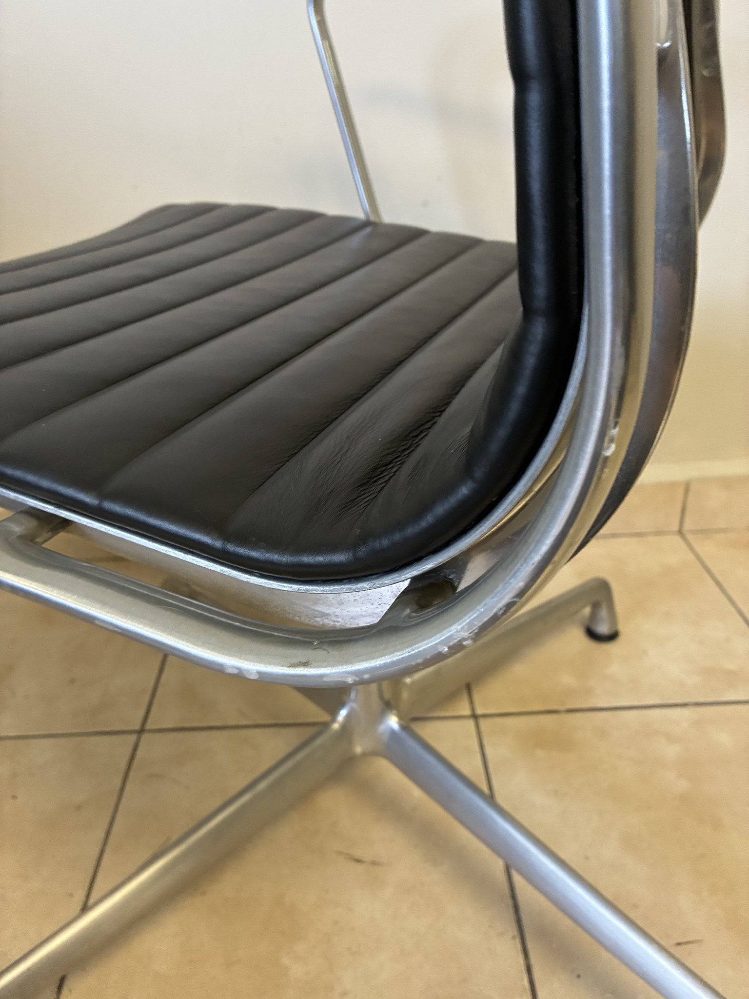 Silla Eames Herman Miller fija de piel negra, vista lateral que muestra el asiento y la base de aluminio.