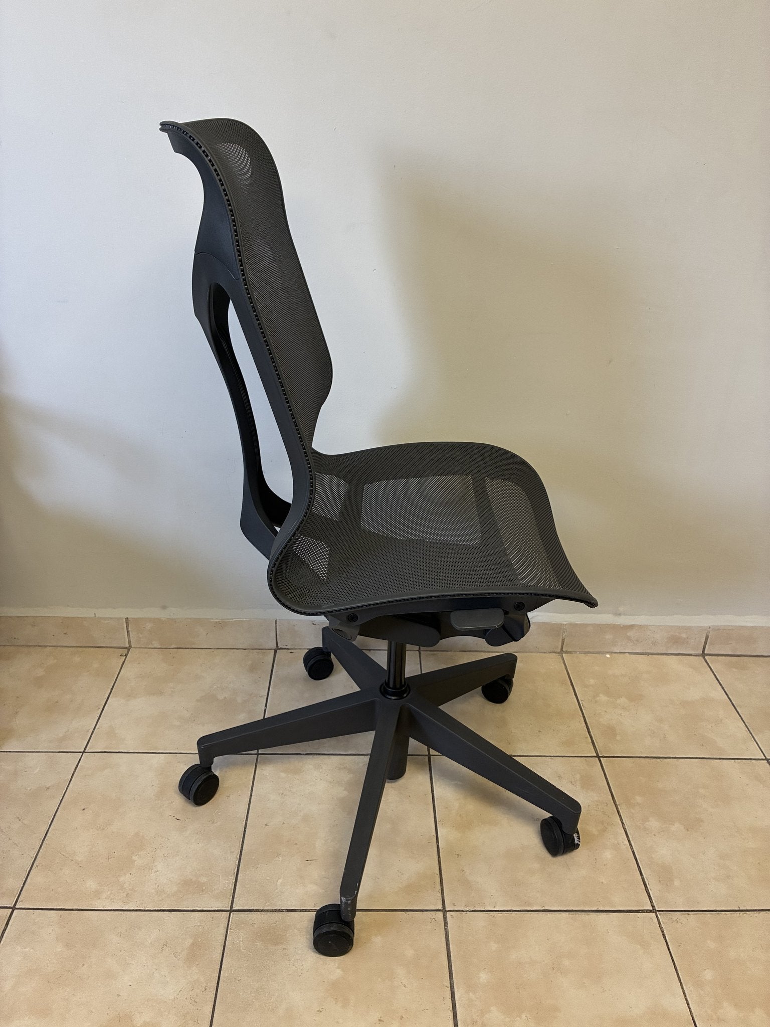 Silla ergonómica Herman Miller Cosm Media color grafito, vista lateral en exhibición, con base de cinco ruedas.
