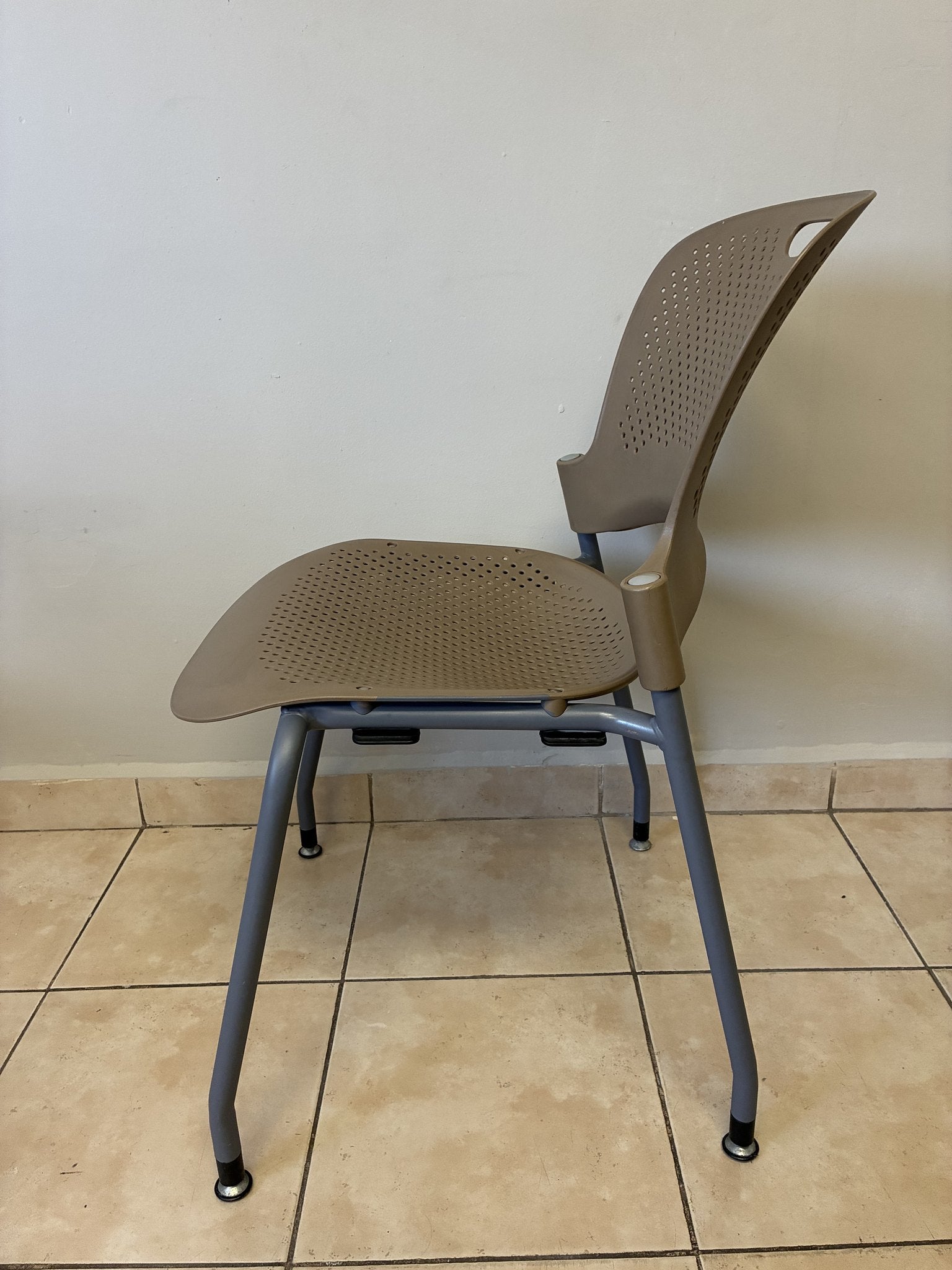 Silla ergonómica Herman Miller Caper en café claro, vista lateral. Asiento y respaldo perforados, patas grises.
