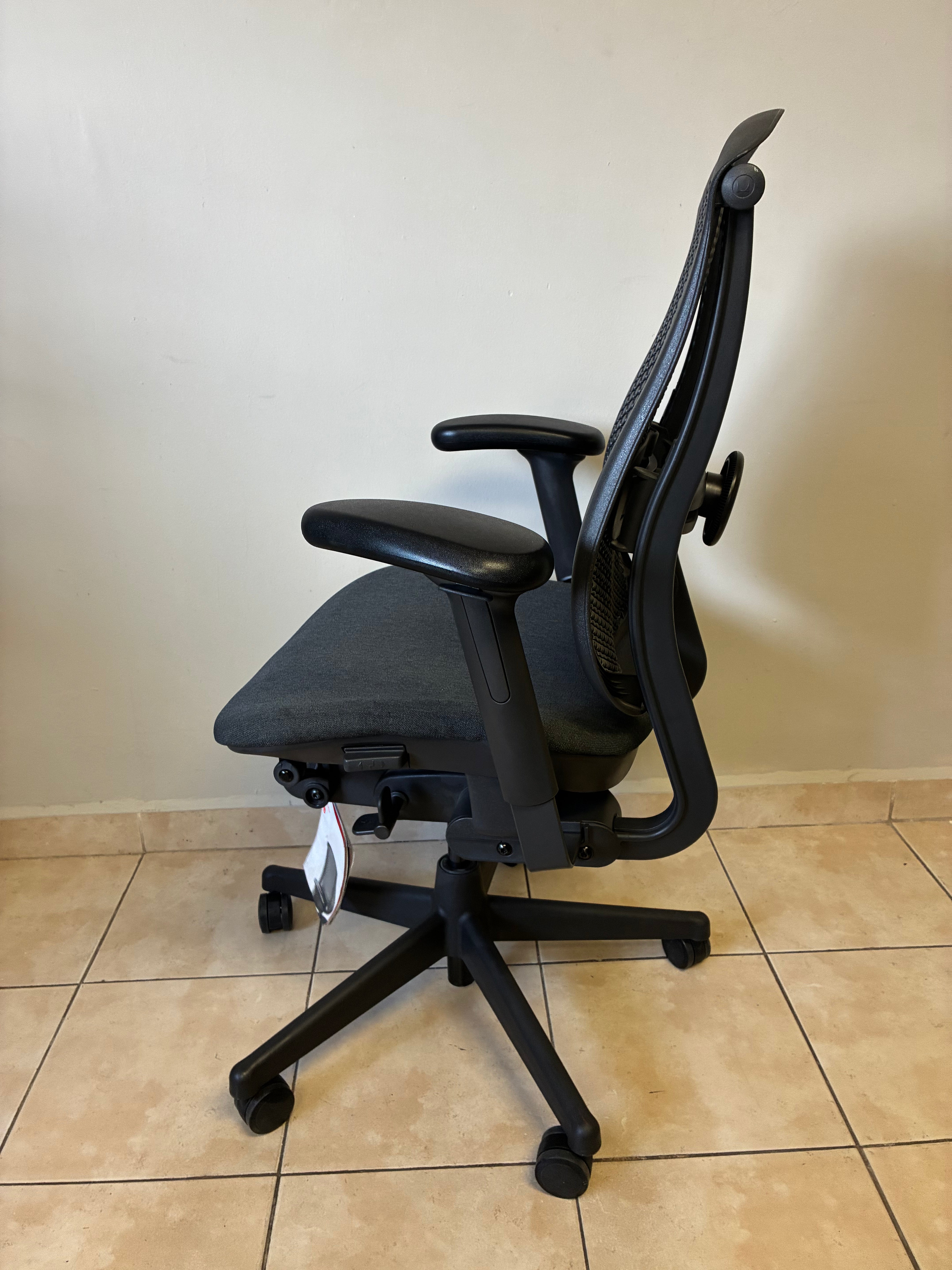 Silla de oficina Herman Miller Celle, equipada y sin uso, en color negro y gris, vista lateral.