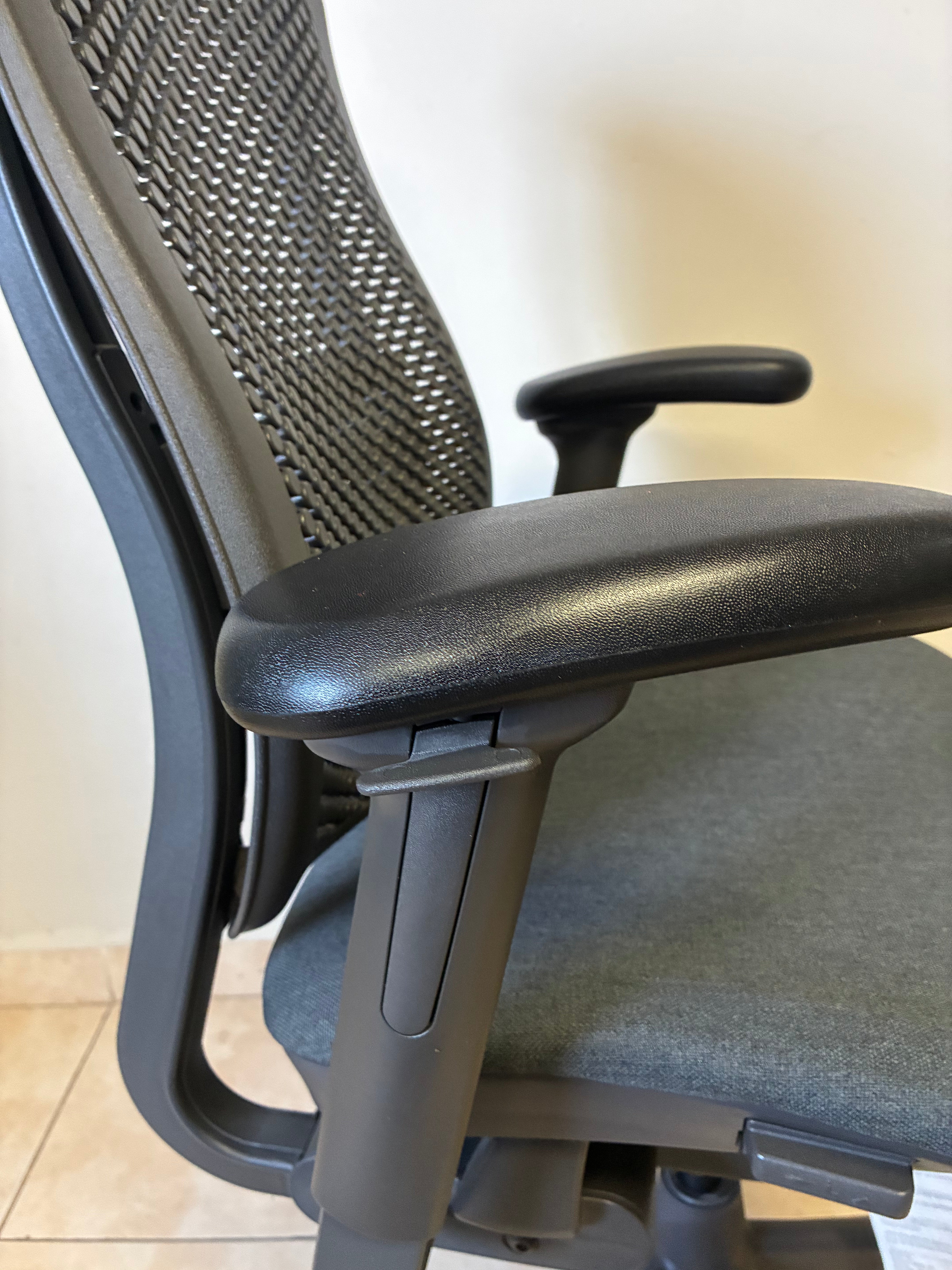 Silla de oficina Herman Miller Celle sin uso, vista lateral de respaldo de malla gris y asiento de tela.