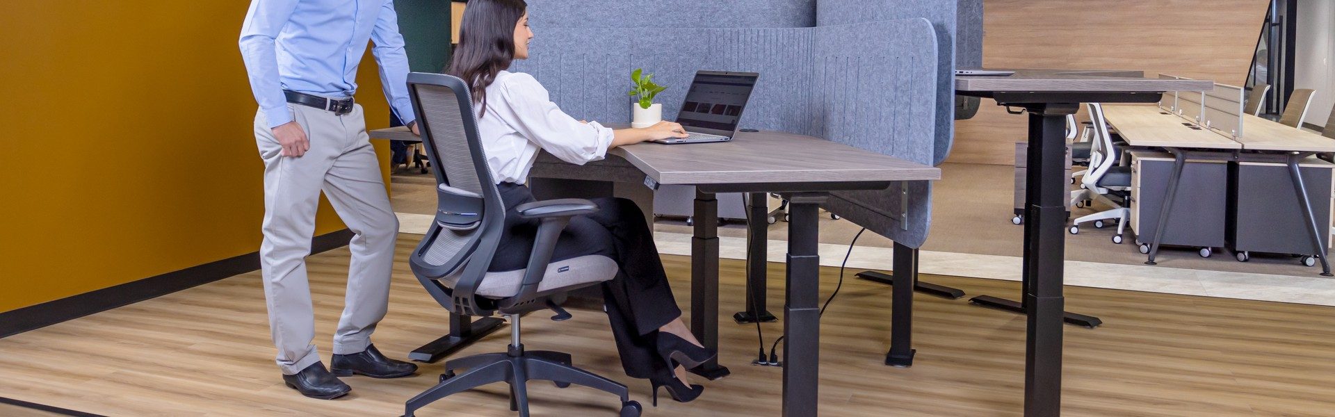 Dos personas en una estación de trabajo con escritorio de altura ajustable y silla ergonómica de malla